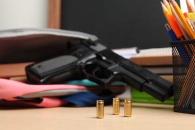 Photo of Gun, bullets and school stationery on wooden table, closeup
