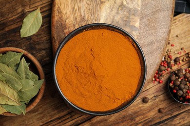 Photo of Bowl with saffron powder, peppercorns and bay leaves on wooden table, flat lay