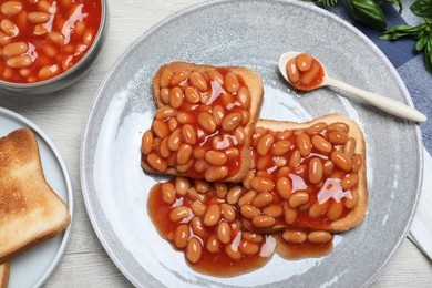 Toasts with delicious canned beans on white wooden table, flat lay