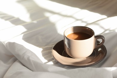 Photo of Cup of aromatic coffee on bed in morning, space for text