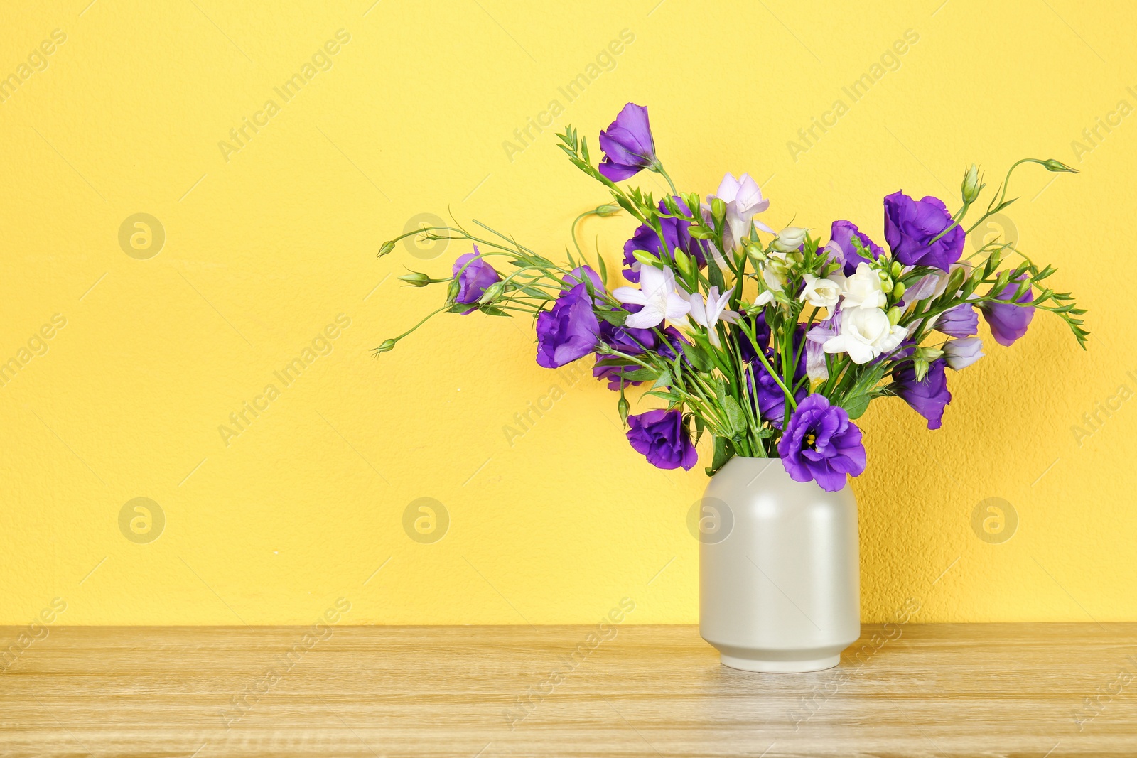 Photo of Vase with beautiful flowers on table against color background. Space for text