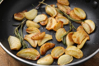 Photo of Frying pan with fried garlic cloves and rosemary, closeup
