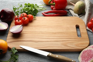 Photo of Cutting board and products on grey wooden table, closeup