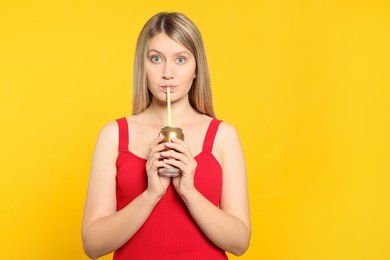 Beautiful woman drinking from beverage can on yellow background