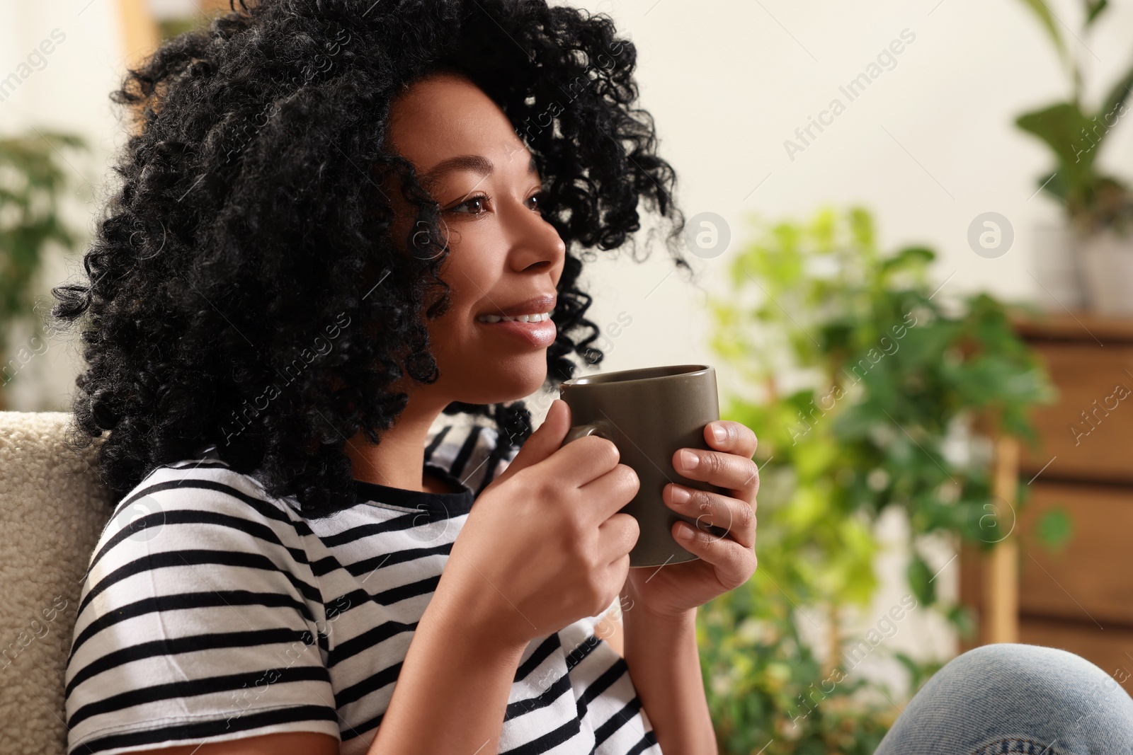 Photo of Relaxing atmosphere. Woman with cup of hot drink sitting near houseplants at home