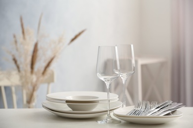 Photo of Set of clean dishware, wineglasses and cutlery on white table indoors