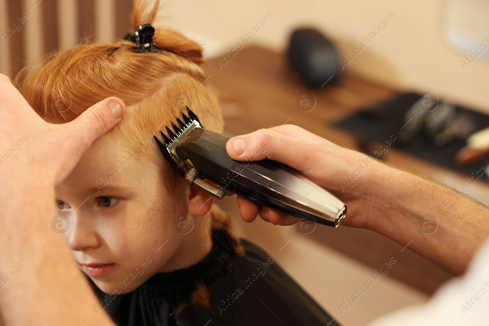 Photo of Professional hairdresser cutting boy's hair in beauty salon, closeup