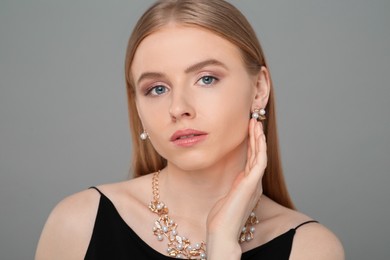 Beautiful young woman with elegant jewelry on gray background