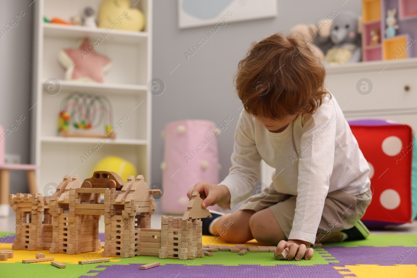 Photo of Little boy playing with wooden construction set on puzzle mat in room. Child's toy