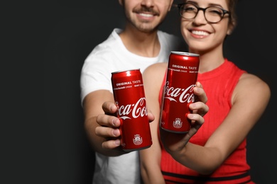 Photo of MYKOLAIV, UKRAINE - NOVEMBER 28, 2018: Young couple with Coca-Cola cans on dark background, closeup