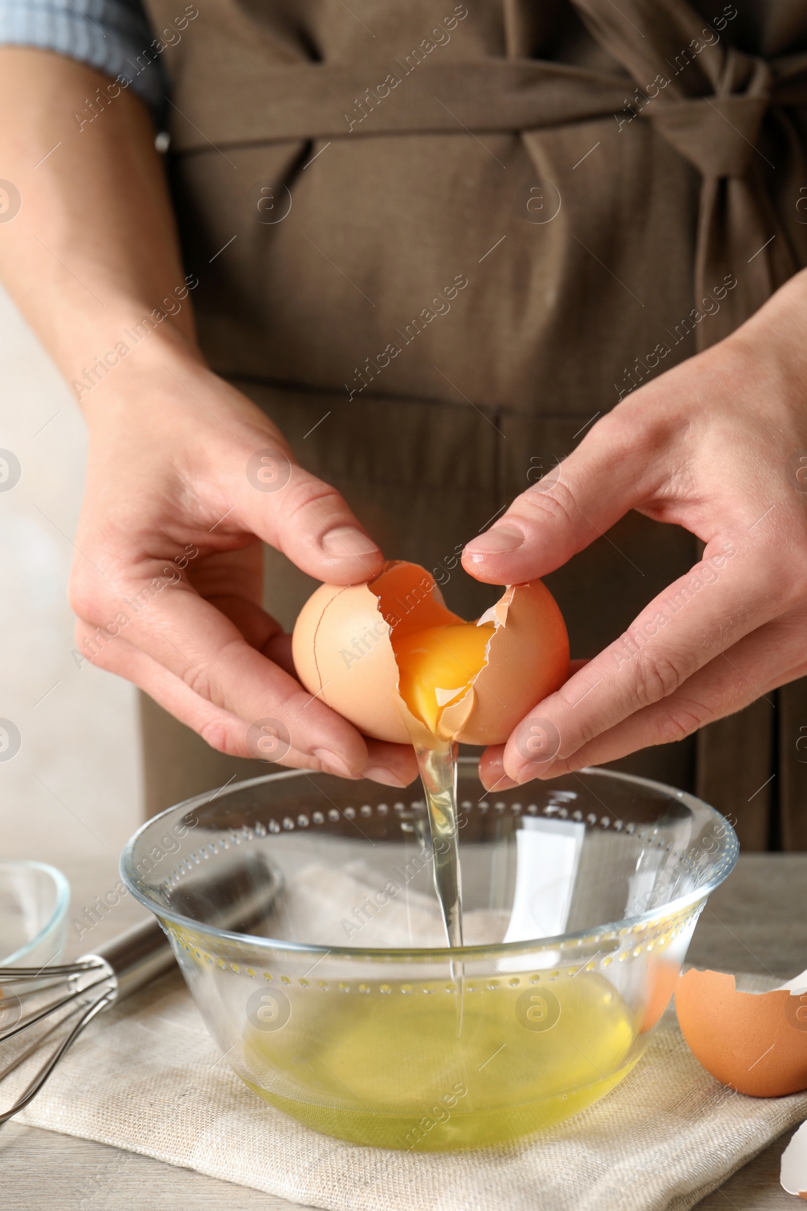 Photo of Woman separating egg yolk from white over glass bowl at light wooden table, closeup