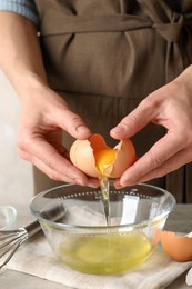 Photo of Woman separating egg yolk from white over glass bowl at light wooden table, closeup