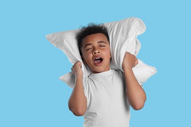 Photo of Boy covering his ears with pillow on light blue background. Insomnia problem