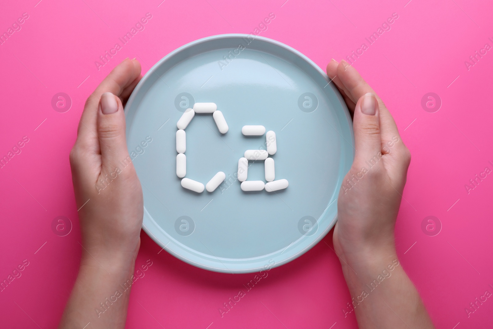 Photo of Woman holding plate with calcium symbol made of white pills on bright pink background, top view