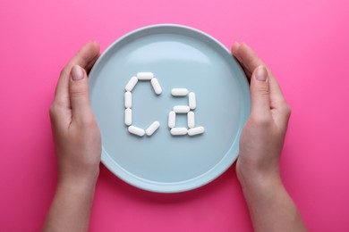 Photo of Woman holding plate with calcium symbol made of white pills on bright pink background, top view