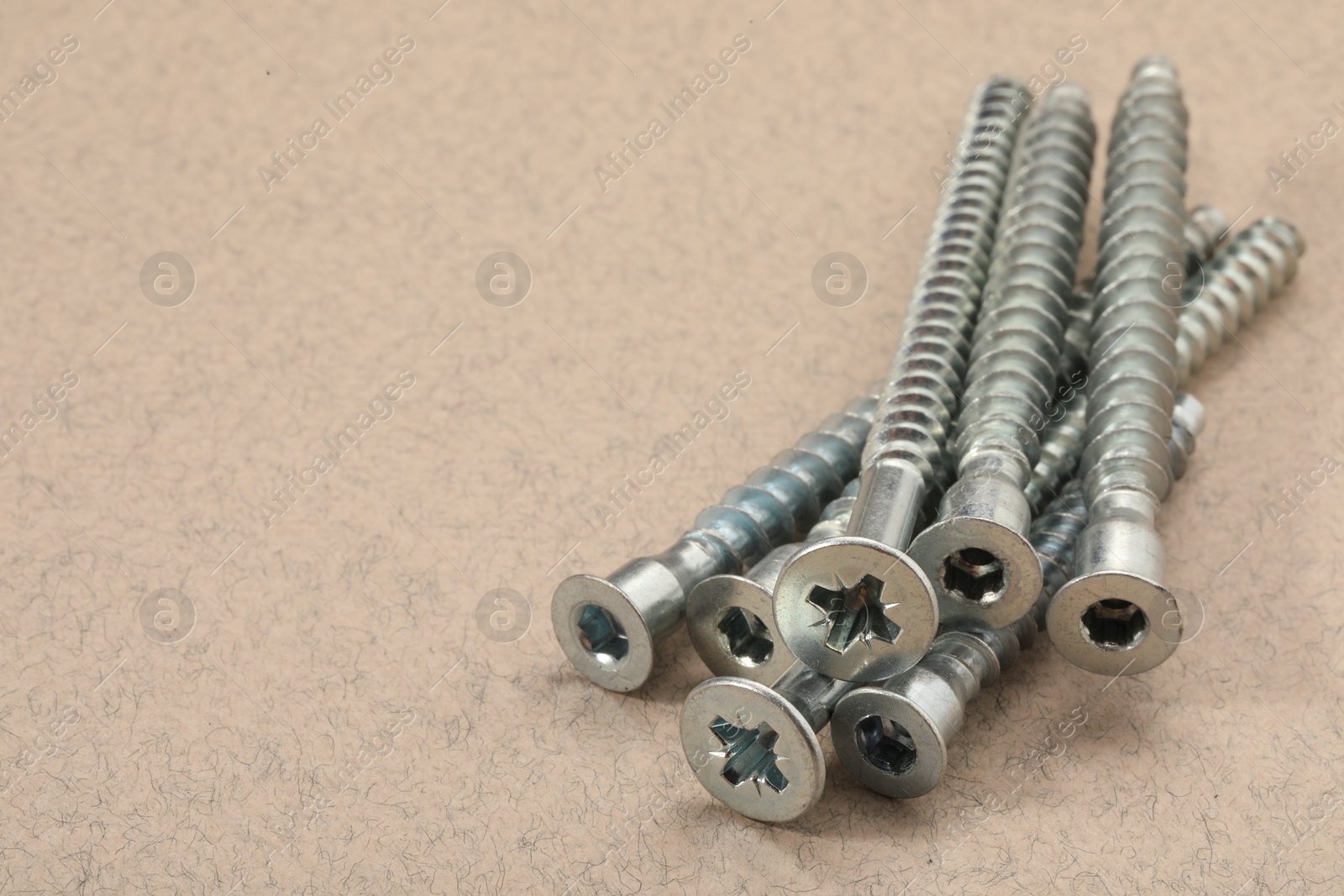 Photo of Many metal screws on beige background, closeup. Space for text