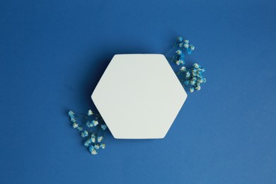 Photo of Product photography prop. Hexagonal shaped podium and flowers on blue background, top view
