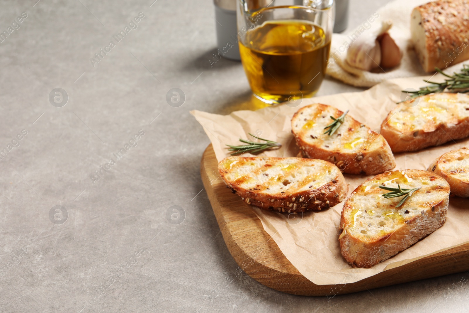 Photo of Tasty bruschettas with oil and rosemary on light grey table, space for text