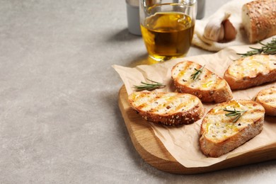 Tasty bruschettas with oil and rosemary on light grey table, space for text