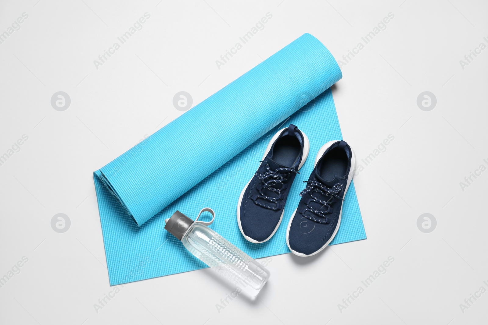 Photo of Exercise mat, bottle of water and shoes on light grey background, flat lay