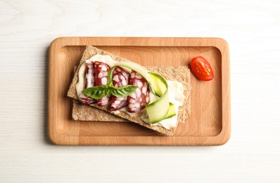 Fresh rye crispbreads with salami, cream cheese and cucumber on white wooden table, top view