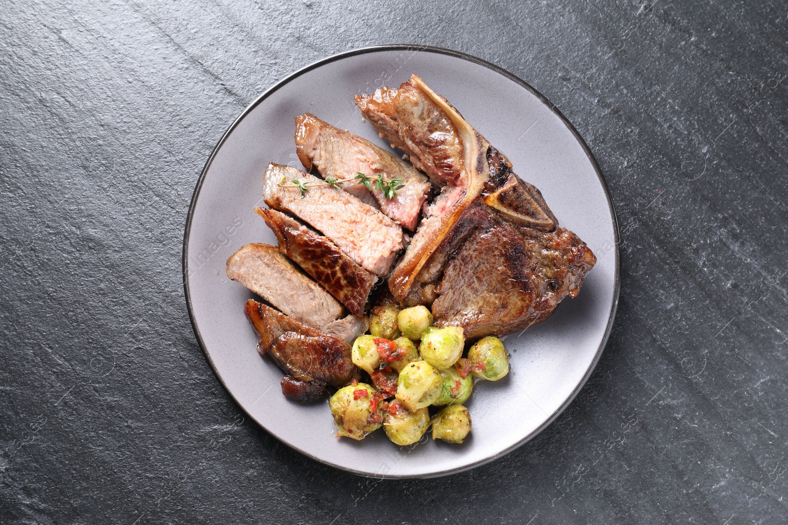 Photo of Delicious fried beef meat, vegetables and thyme on black table, top view