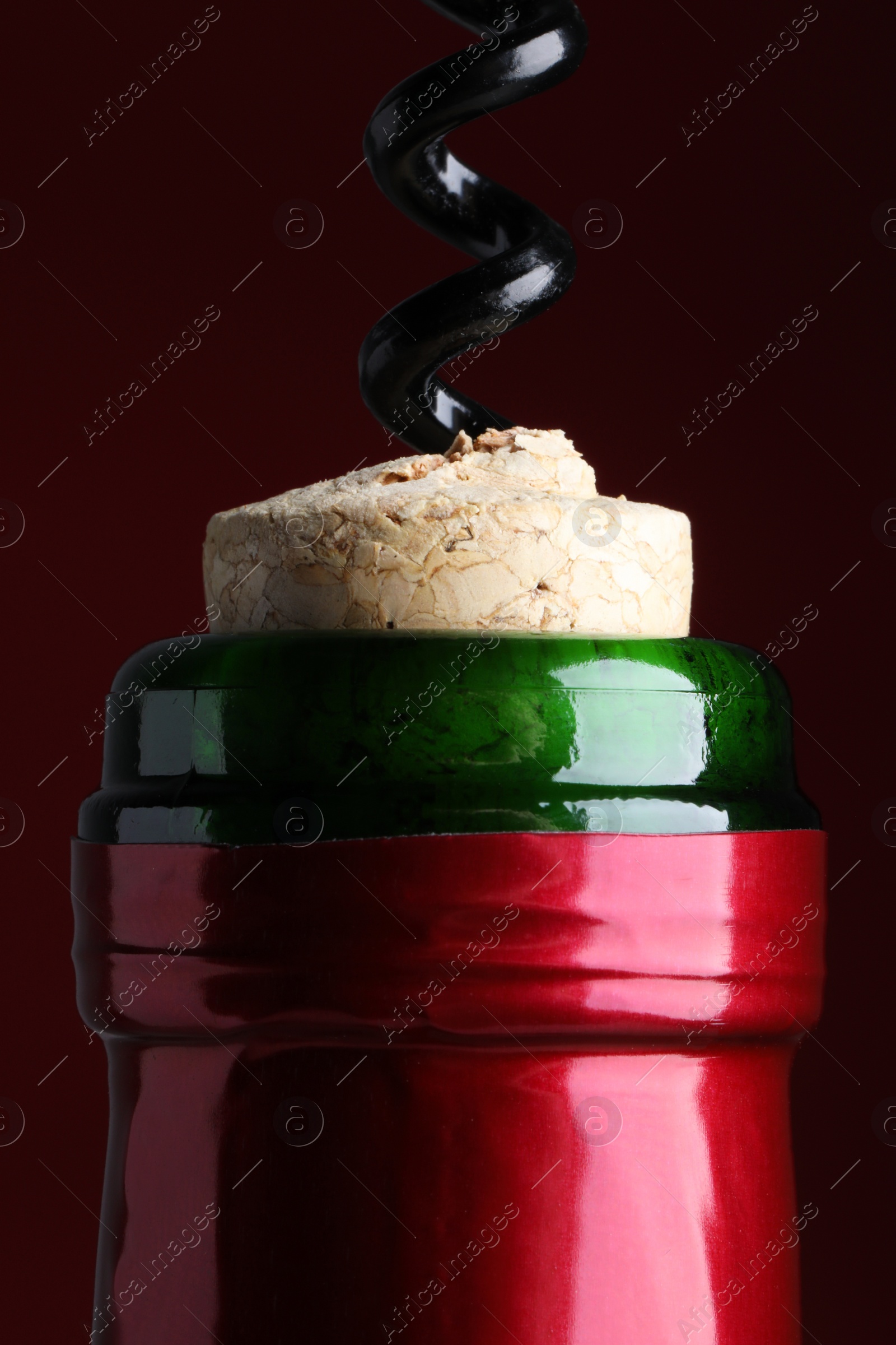 Photo of Opening bottle of wine with corkscrew on burgundy background, closeup