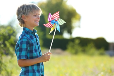 Photo of Cute little boy with pinwheel outdoors, space for text. Child spending time in nature