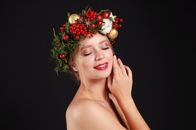 Photo of Beautiful young woman wearing Christmas wreath on black background