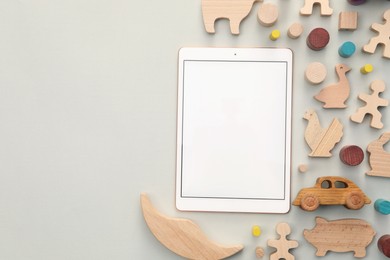 Modern tablet and wooden toys on light background, flat lay. Space for text