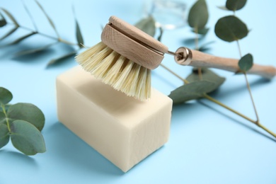 Cleaning brush and soap bar for dish washing on light blue background, closeup