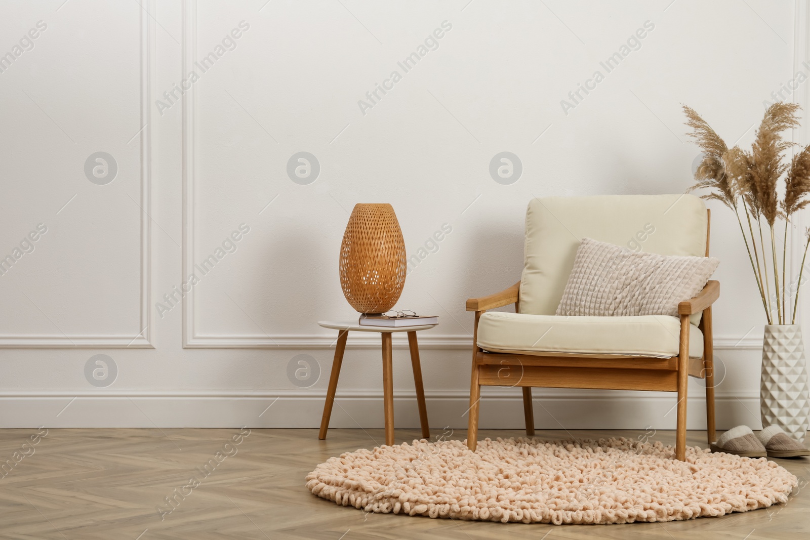 Photo of Stylish armchair with cushion and lamp near white wall indoors, space for text. Interior design