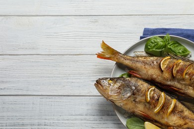 Photo of Tasty homemade roasted perches on white wooden table, top view and space for text. River fish