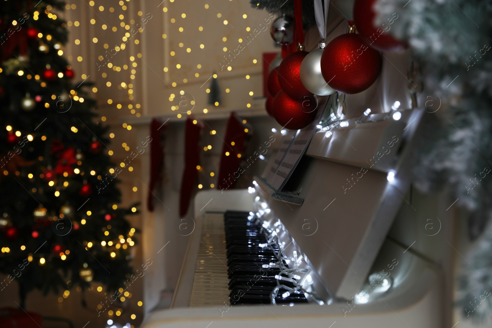 Photo of White piano with fairy lights and baubles indoors, space for text. Christmas music