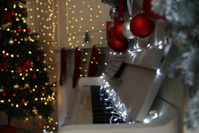White piano with fairy lights and baubles indoors, space for text. Christmas music