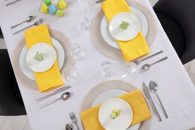 Photo of Festive table setting with glasses, painted eggs and plates, view from above. Easter celebration