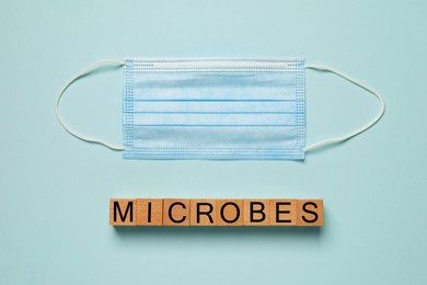 Photo of Word Microbes made with wooden cubes and face mask on turquoise background, flat lay