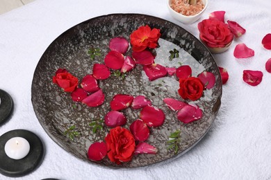 Photo of Plate with water, rose petals and sea salt on white towel. Pedicure procedure