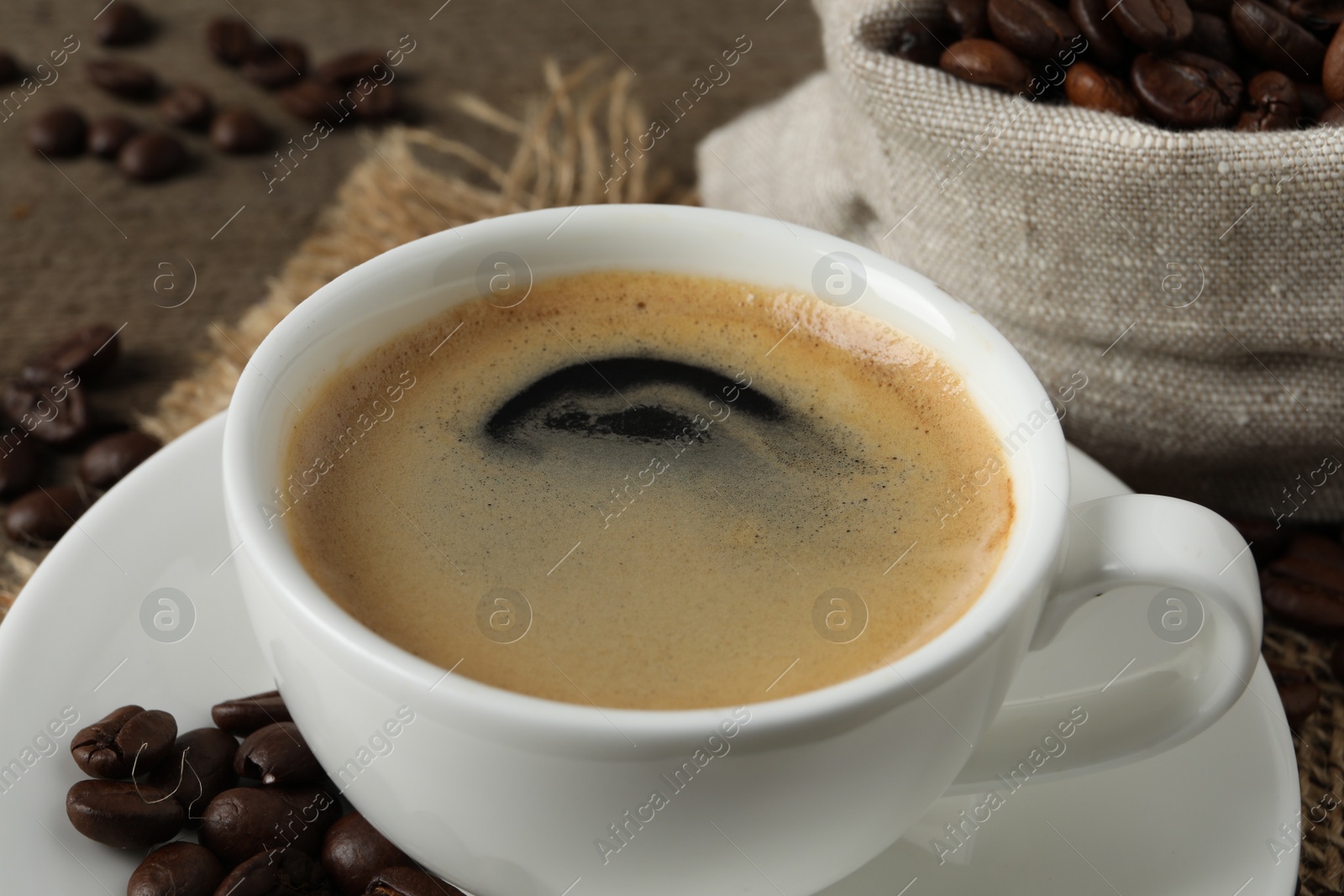 Photo of Cup of aromatic coffee and beans on wooden table, closeup