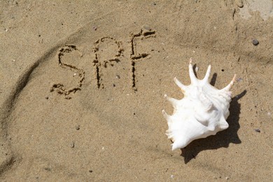 Abbreviation SPF written on sand and seashell at beach, top view