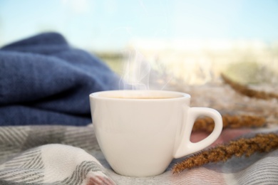 Image of Cup of hot drink and blanket on window sill indoors