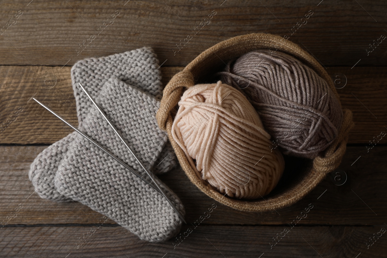 Photo of Soft colorful yarns, knitted socks and metal needles on wooden table, flat lay