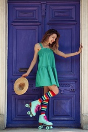 Photo of Happy girl with retro roller skates standing near violet door