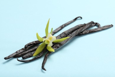Photo of Vanilla pods and beautiful flower on light blue background, closeup