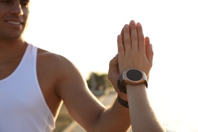 Photo of Couple with fitness trackers giving each other high fives after training outdoors, closeup