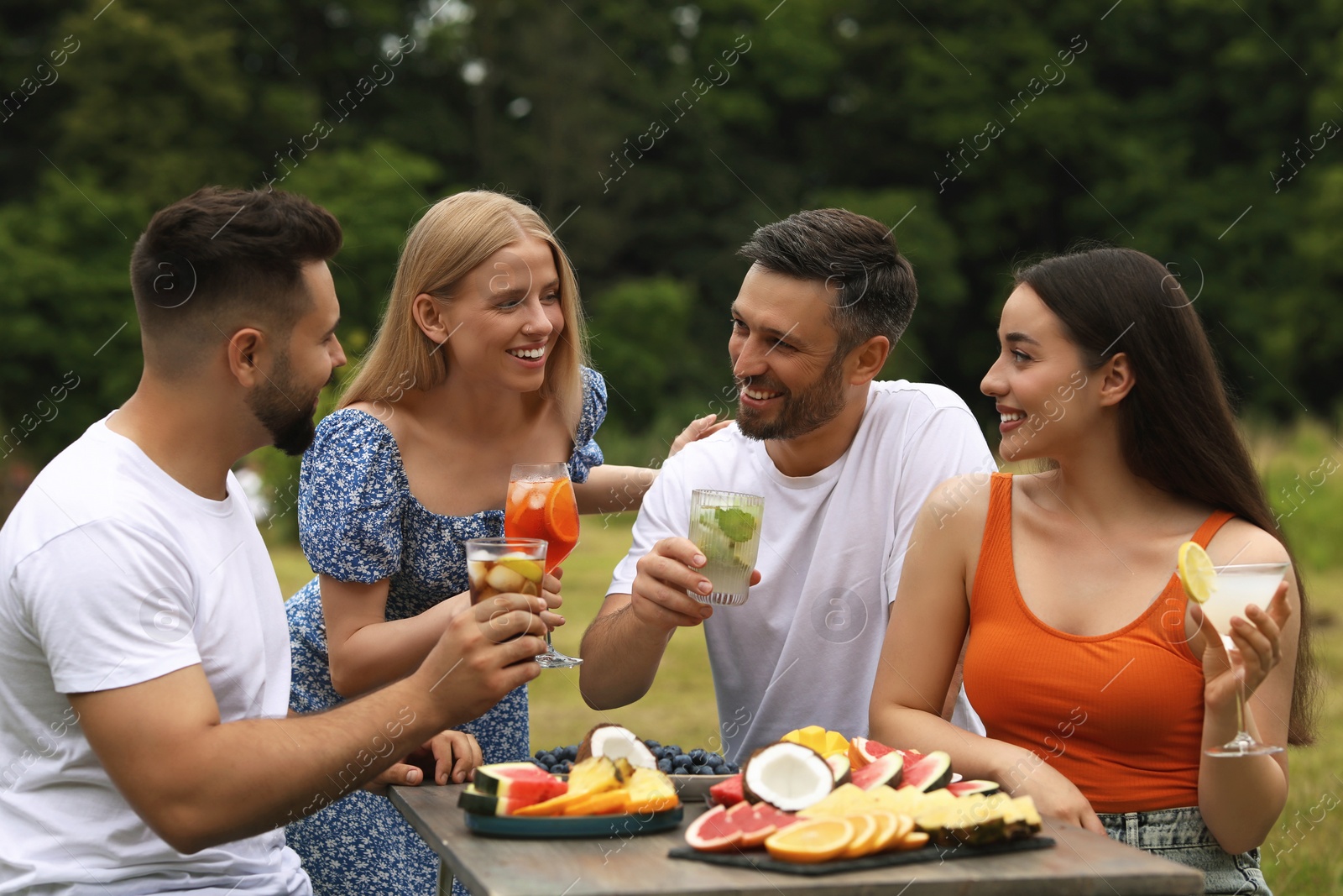 Photo of Happy friends with glasses of cocktails at table outdoors