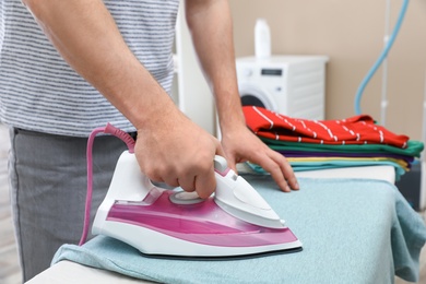 Photo of Man ironing clothes on board at home, closeup