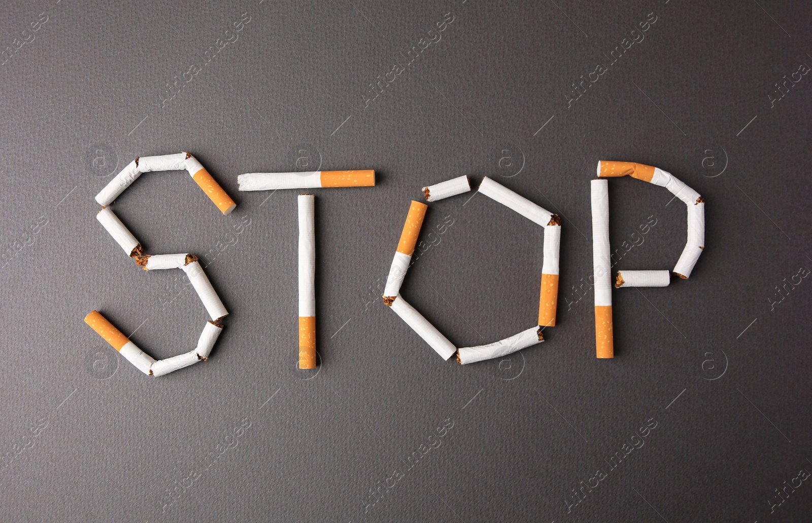 Photo of Word Stop made of cigarettes on dark grey background, top view. Quitting smoking concept