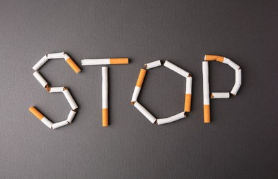 Photo of Word Stop made of cigarettes on dark grey background, top view. Quitting smoking concept