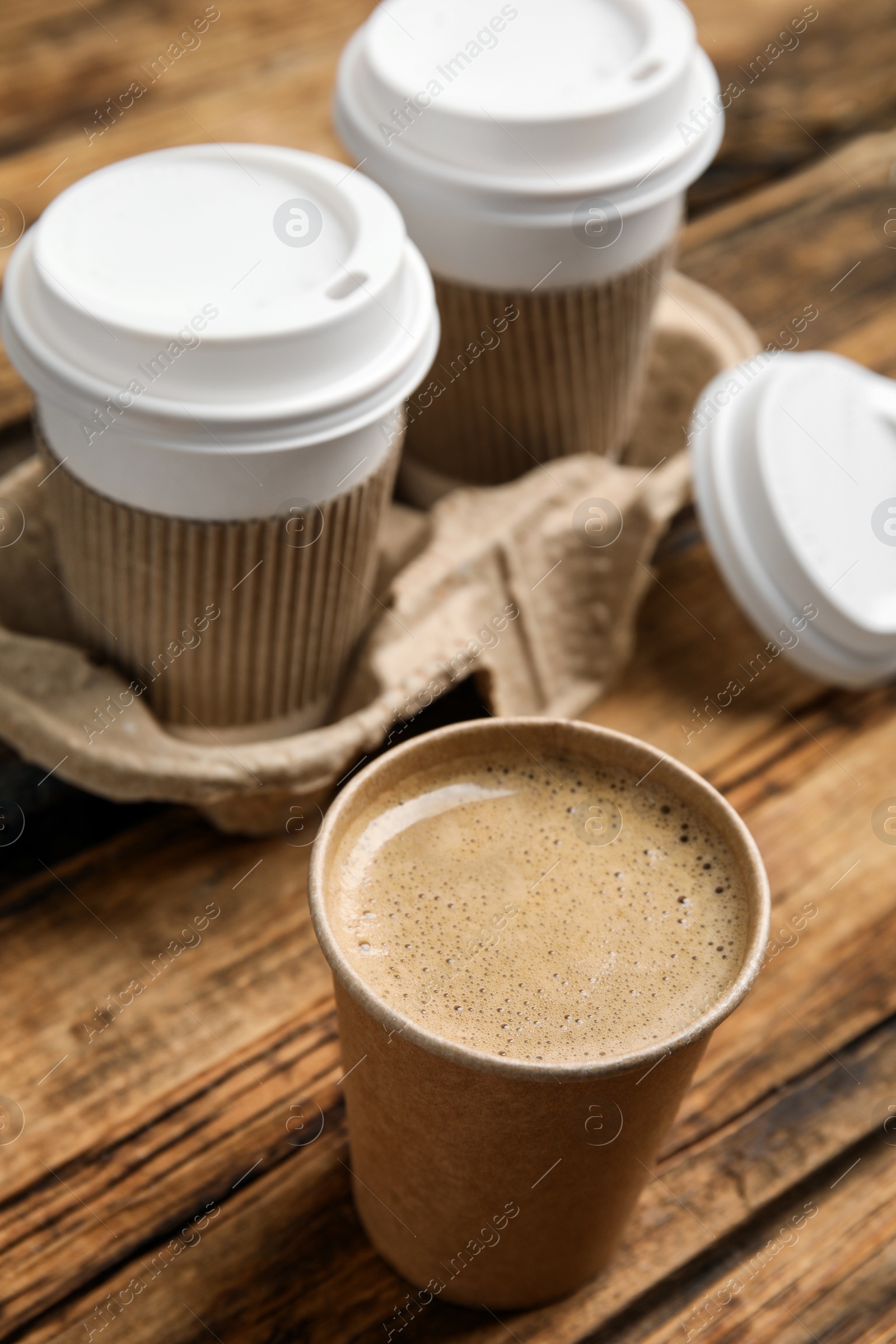 Photo of Takeaway paper cups with coffee and cardboard holder on wooden table